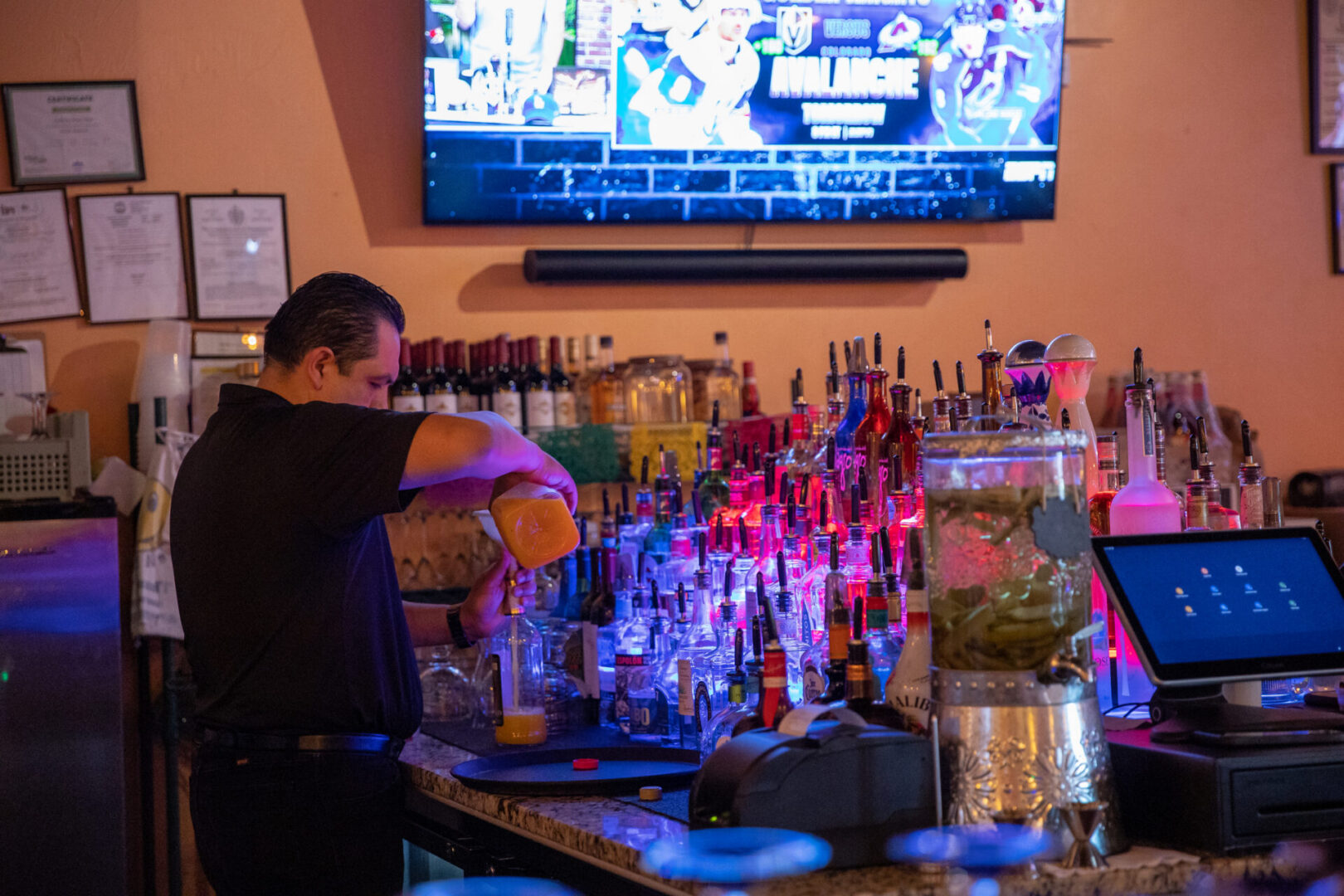 Bartender pouring drink at colorful backlit bar